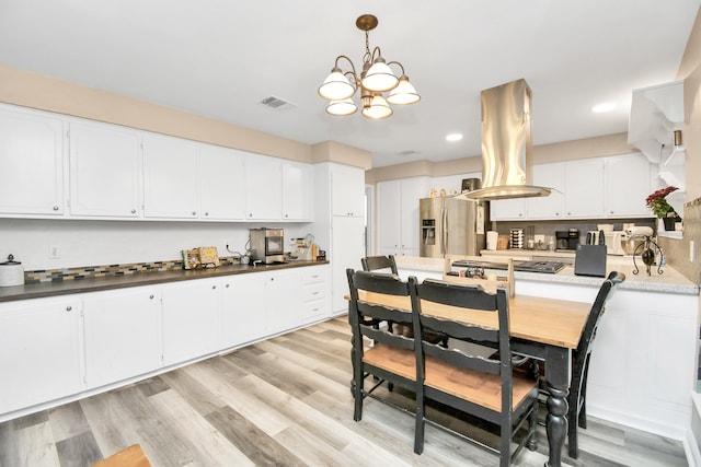 kitchen with stainless steel appliances, light hardwood / wood-style floors, white cabinetry, an inviting chandelier, and island exhaust hood