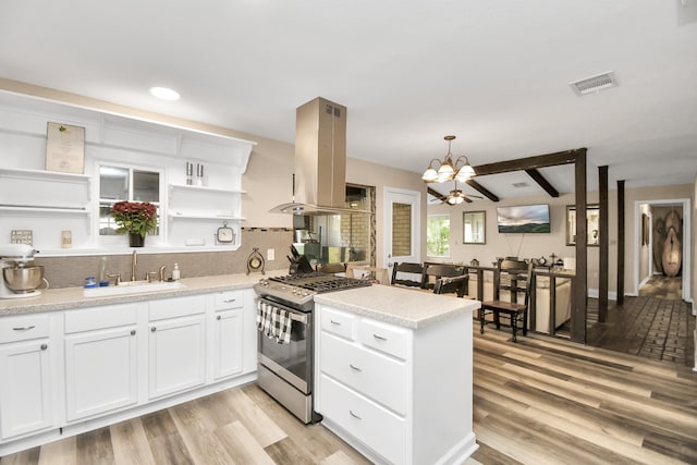 kitchen with white cabinets, stainless steel range with gas stovetop, sink, island exhaust hood, and decorative light fixtures