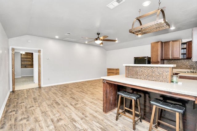 kitchen with ceiling fan, light hardwood / wood-style flooring, backsplash, a breakfast bar, and vaulted ceiling