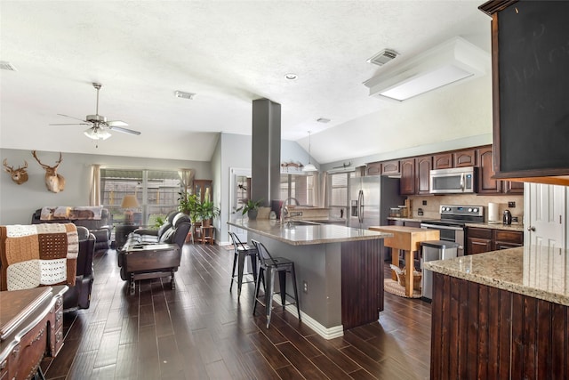 kitchen featuring dark brown cabinetry, lofted ceiling, dark wood-type flooring, stainless steel appliances, and a breakfast bar area