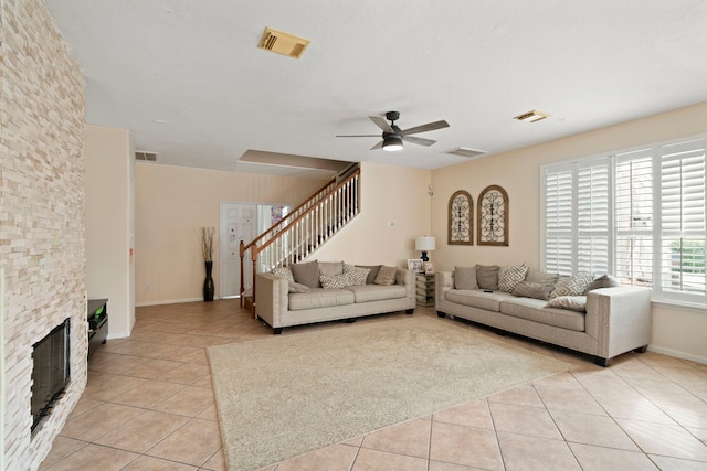 living room with ceiling fan, a stone fireplace, and light tile patterned floors