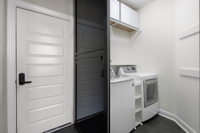 washroom featuring washer and dryer, dark tile patterned flooring, and cabinets