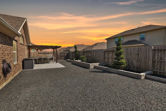 yard at dusk with a fenced backyard, a pergola, and a patio area