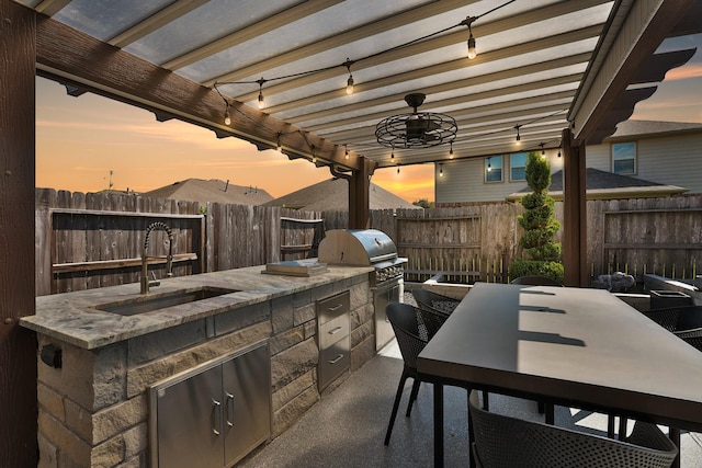 patio terrace at dusk featuring an outdoor kitchen, outdoor dining area, a fenced backyard, a pergola, and a sink