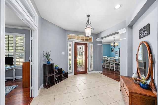 foyer with ornamental molding, light hardwood / wood-style floors, a chandelier, and decorative columns