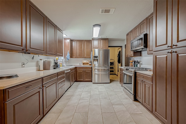 kitchen featuring stainless steel appliances, sink, light tile patterned floors, and a textured ceiling