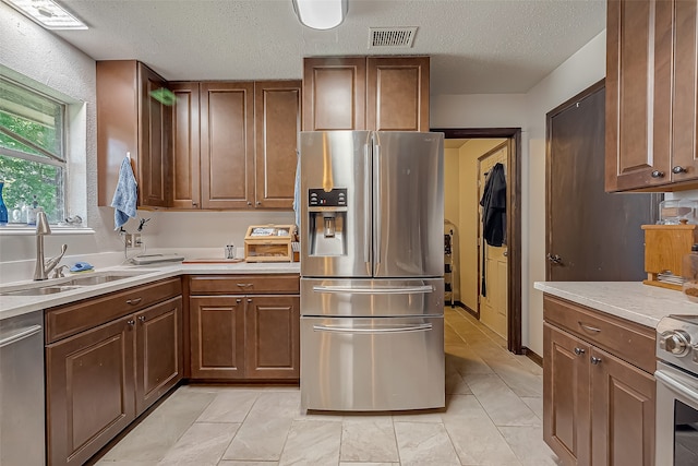 kitchen with appliances with stainless steel finishes, sink, light tile patterned floors, and a textured ceiling