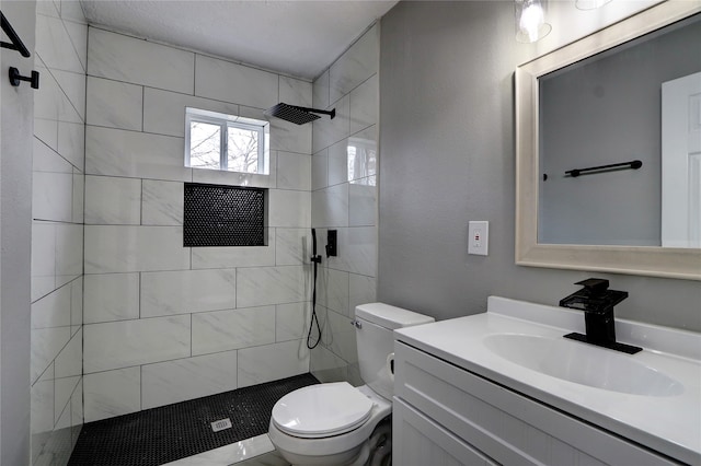 bathroom with a tile shower, vanity, and toilet