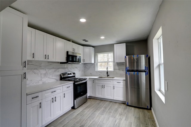 kitchen featuring stainless steel appliances, backsplash, sink, and white cabinetry