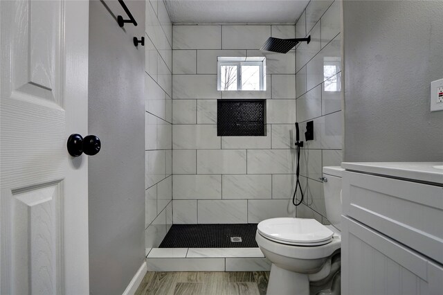 bathroom with a tile shower, hardwood / wood-style floors, vanity, and toilet