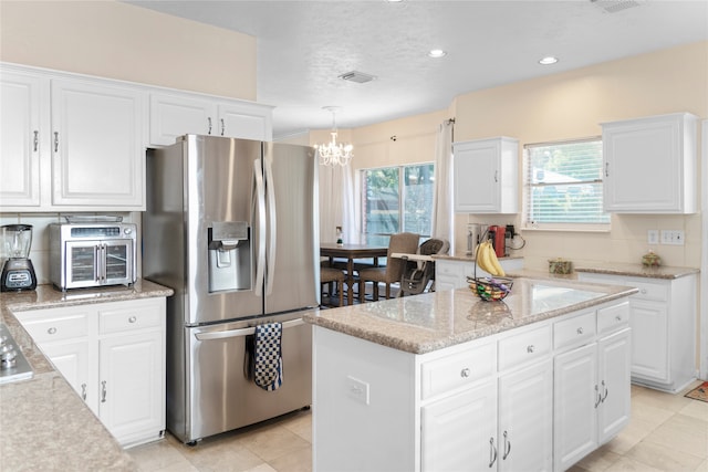 kitchen featuring stainless steel fridge, pendant lighting, white cabinetry, and a kitchen island