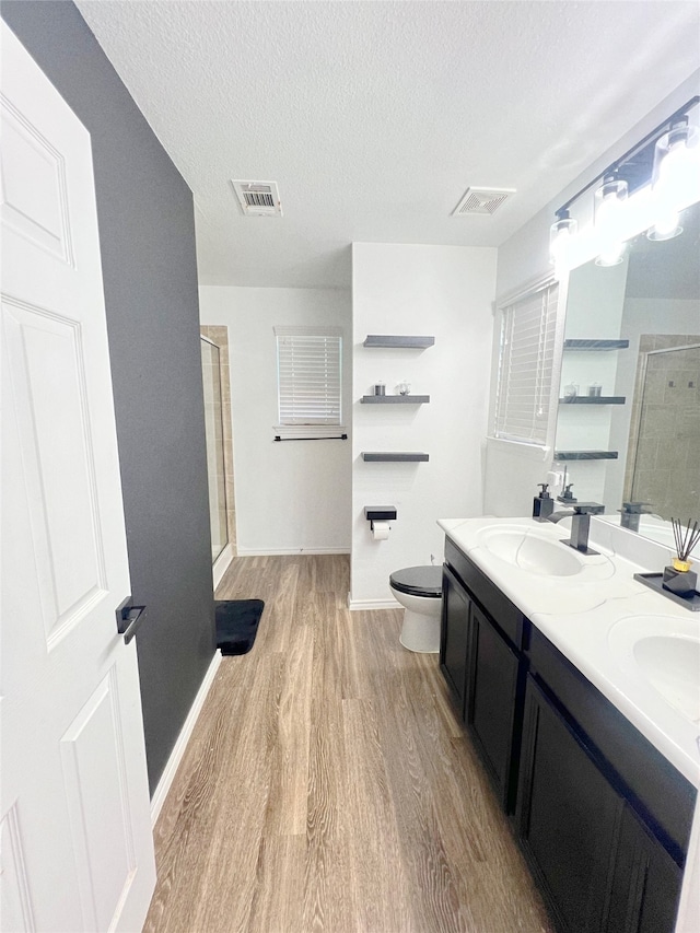 bathroom with walk in shower, toilet, wood-type flooring, vanity, and a textured ceiling