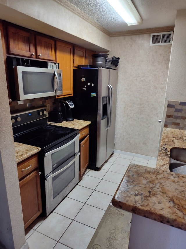 kitchen featuring light tile patterned floors, appliances with stainless steel finishes, a textured ceiling, crown molding, and light stone counters