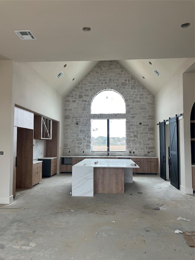 kitchen with a barn door, a kitchen island, and high vaulted ceiling