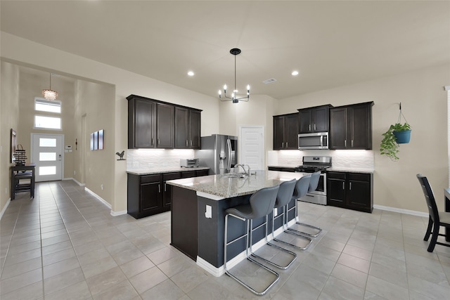 kitchen featuring decorative backsplash, a kitchen island with sink, light tile patterned flooring, appliances with stainless steel finishes, and a kitchen bar