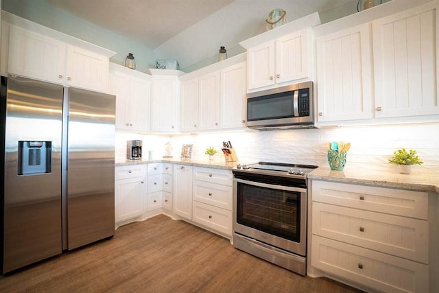 kitchen featuring light wood-type flooring, light stone counters, stainless steel appliances, white cabinets, and backsplash