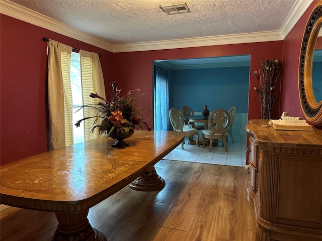 dining area featuring a textured ceiling, light wood-type flooring, and crown molding