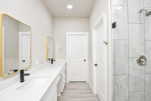 bathroom with a sink, tiled shower, wood finished floors, and double vanity