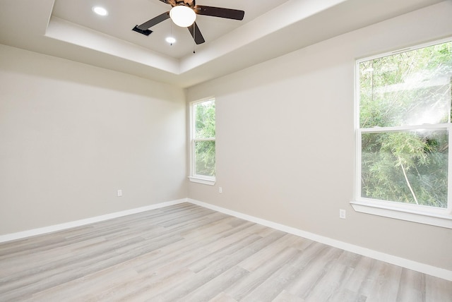 spare room featuring baseboards, a tray ceiling, light wood-style flooring, recessed lighting, and ceiling fan