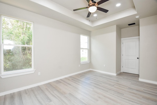 unfurnished room with a raised ceiling, recessed lighting, baseboards, and light wood-type flooring