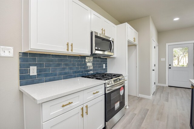 kitchen featuring backsplash, light stone countertops, light wood-style flooring, white cabinets, and stainless steel appliances