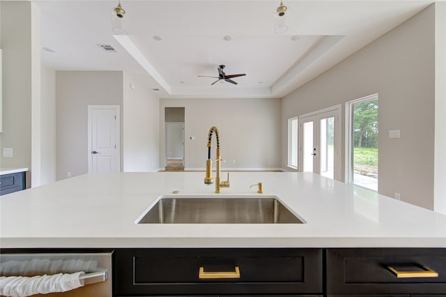 kitchen featuring ceiling fan, french doors, a raised ceiling, sink, and a center island with sink