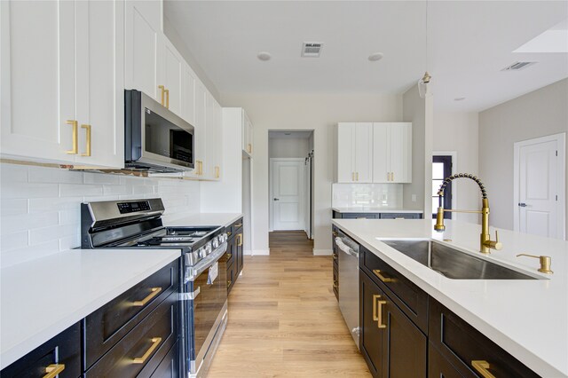 kitchen with white cabinets, light hardwood / wood-style floors, appliances with stainless steel finishes, and sink