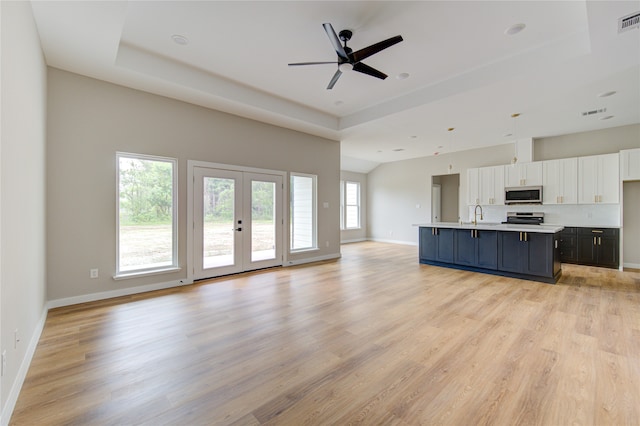 unfurnished living room featuring light wood-type flooring, ceiling fan, a raised ceiling, sink, and french doors