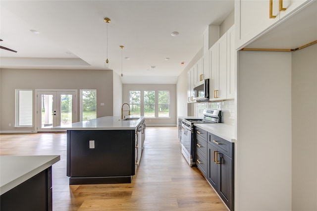 kitchen featuring appliances with stainless steel finishes, decorative light fixtures, a kitchen island with sink, and white cabinets