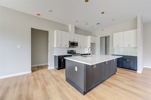 kitchen with pendant lighting, tasteful backsplash, an island with sink, appliances with stainless steel finishes, and white cabinetry