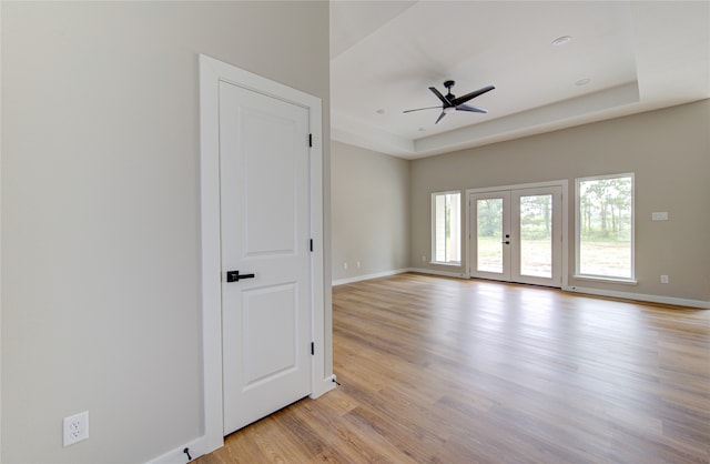 empty room featuring a raised ceiling, french doors, light wood-type flooring, and ceiling fan