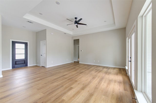 unfurnished living room with ceiling fan, a tray ceiling, and light hardwood / wood-style floors