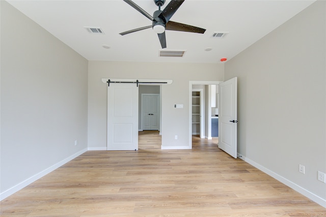 unfurnished bedroom featuring ceiling fan, light hardwood / wood-style floors, and a barn door