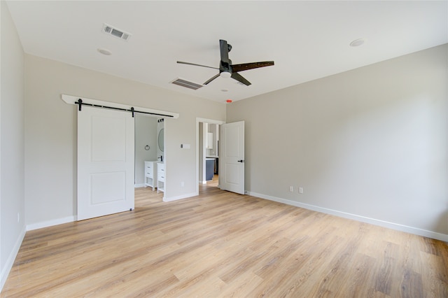 unfurnished bedroom with light wood-type flooring, ceiling fan, and a barn door