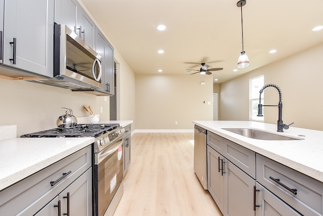 kitchen featuring light wood-type flooring, stainless steel appliances, gray cabinetry, sink, and hanging light fixtures