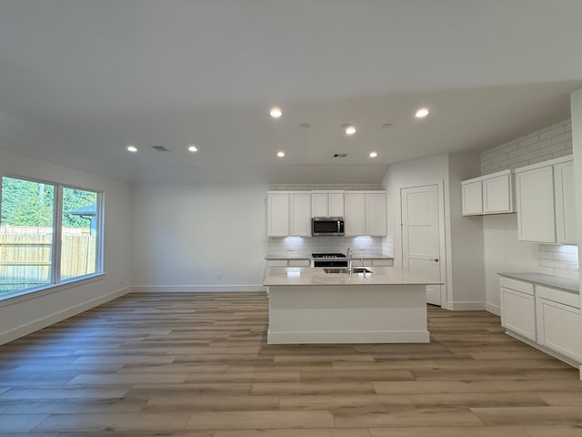 kitchen featuring backsplash, a center island with sink, appliances with stainless steel finishes, light hardwood / wood-style floors, and white cabinetry