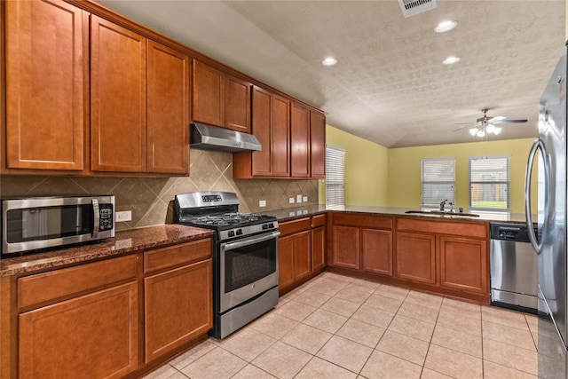 kitchen with dark stone counters, appliances with stainless steel finishes, light tile patterned floors, sink, and ceiling fan