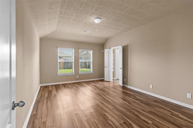 spare room with hardwood / wood-style floors, a textured ceiling, and vaulted ceiling