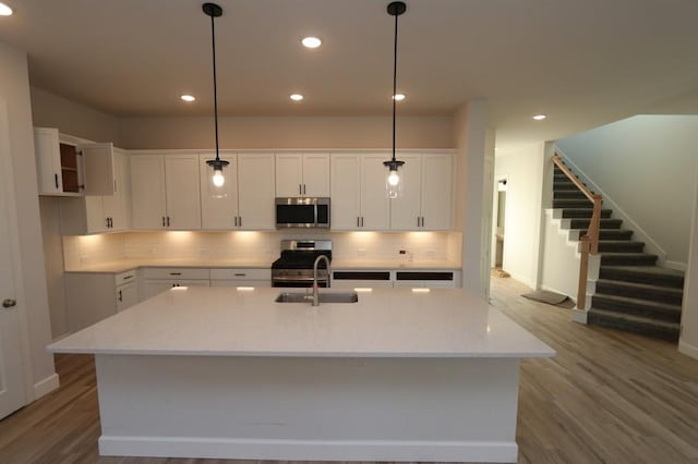 kitchen with decorative light fixtures, a center island with sink, sink, stainless steel appliances, and white cabinets