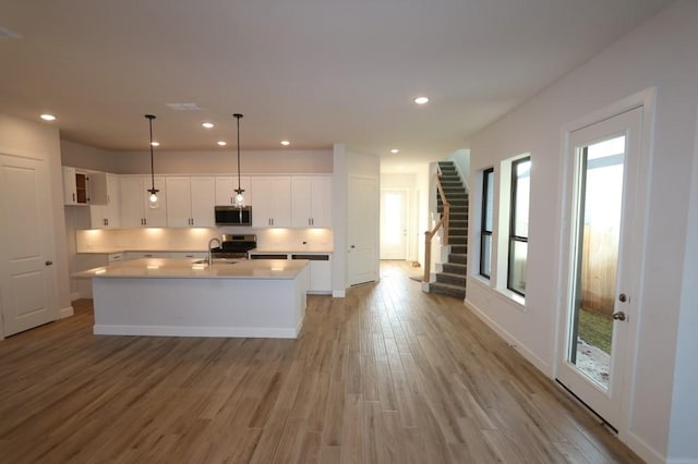 kitchen featuring decorative light fixtures, white cabinetry, stainless steel appliances, a kitchen island with sink, and light hardwood / wood-style flooring