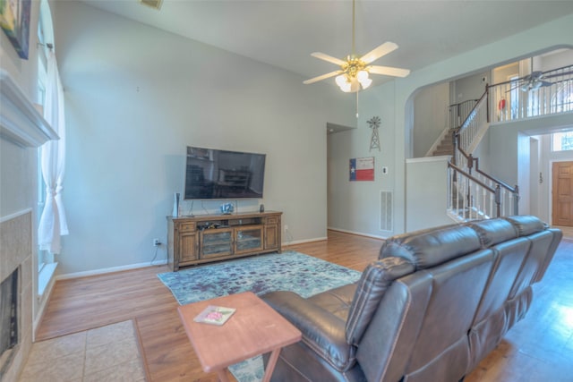 living room with a tile fireplace, ceiling fan, a high ceiling, and light wood-type flooring