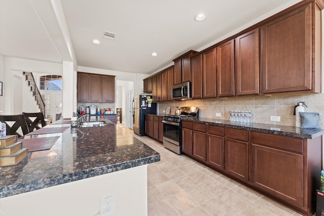 kitchen with dark stone countertops, appliances with stainless steel finishes, sink, and decorative backsplash