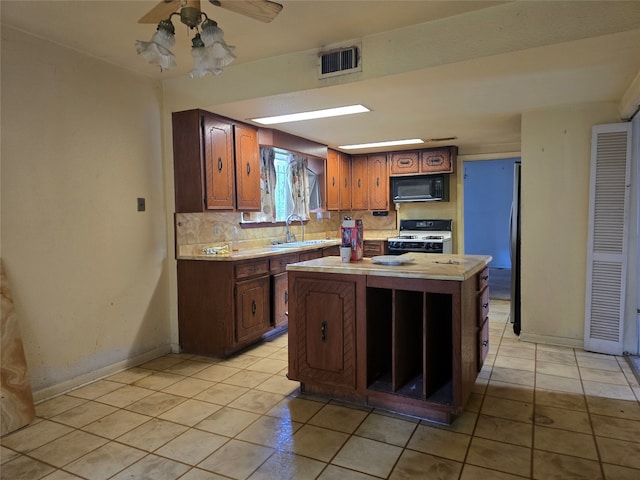 kitchen featuring a kitchen island, gas range gas stove, sink, decorative backsplash, and light tile patterned floors