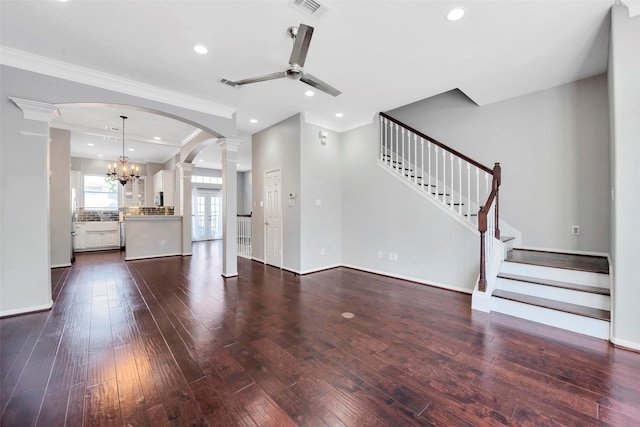 unfurnished living room with ceiling fan with notable chandelier, crown molding, ornate columns, and dark wood-type flooring