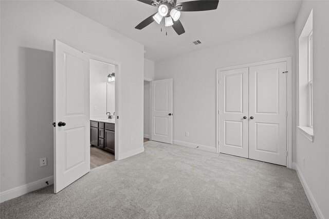 unfurnished bedroom featuring a closet, ensuite bathroom, light carpet, and ceiling fan