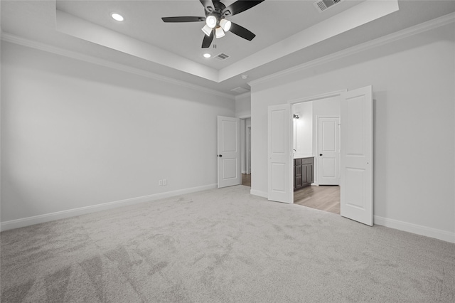 unfurnished bedroom featuring ensuite bathroom, a tray ceiling, crown molding, ceiling fan, and light carpet