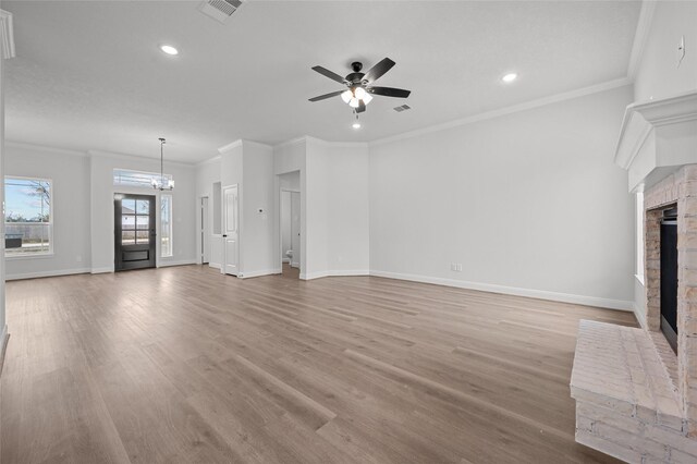 unfurnished living room with ornamental molding, light wood-type flooring, a brick fireplace, and ceiling fan with notable chandelier