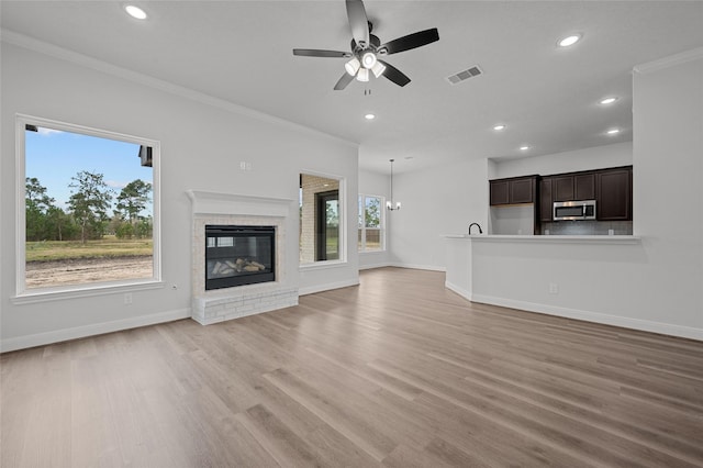 unfurnished living room featuring ceiling fan with notable chandelier, a brick fireplace, ornamental molding, and light wood-type flooring