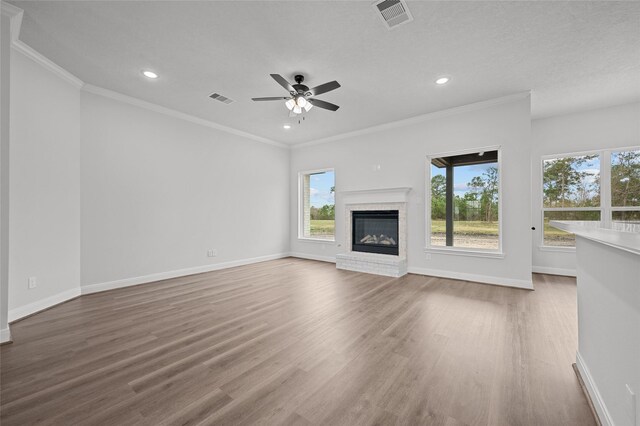 unfurnished living room featuring a brick fireplace, ceiling fan, crown molding, and hardwood / wood-style floors