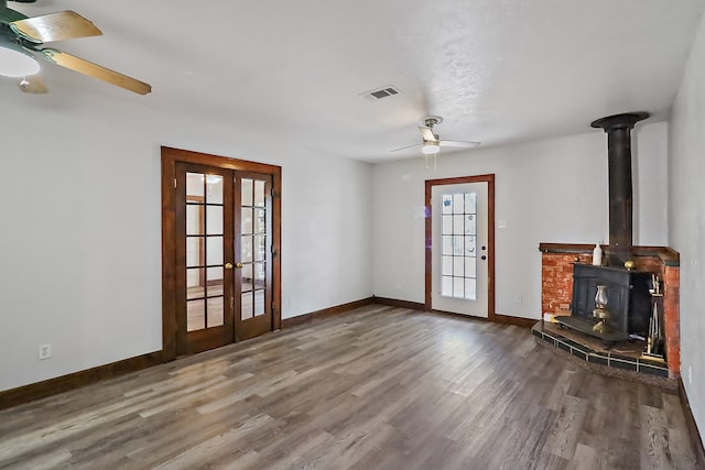 unfurnished living room with french doors, ceiling fan, a wood stove, and hardwood / wood-style floors